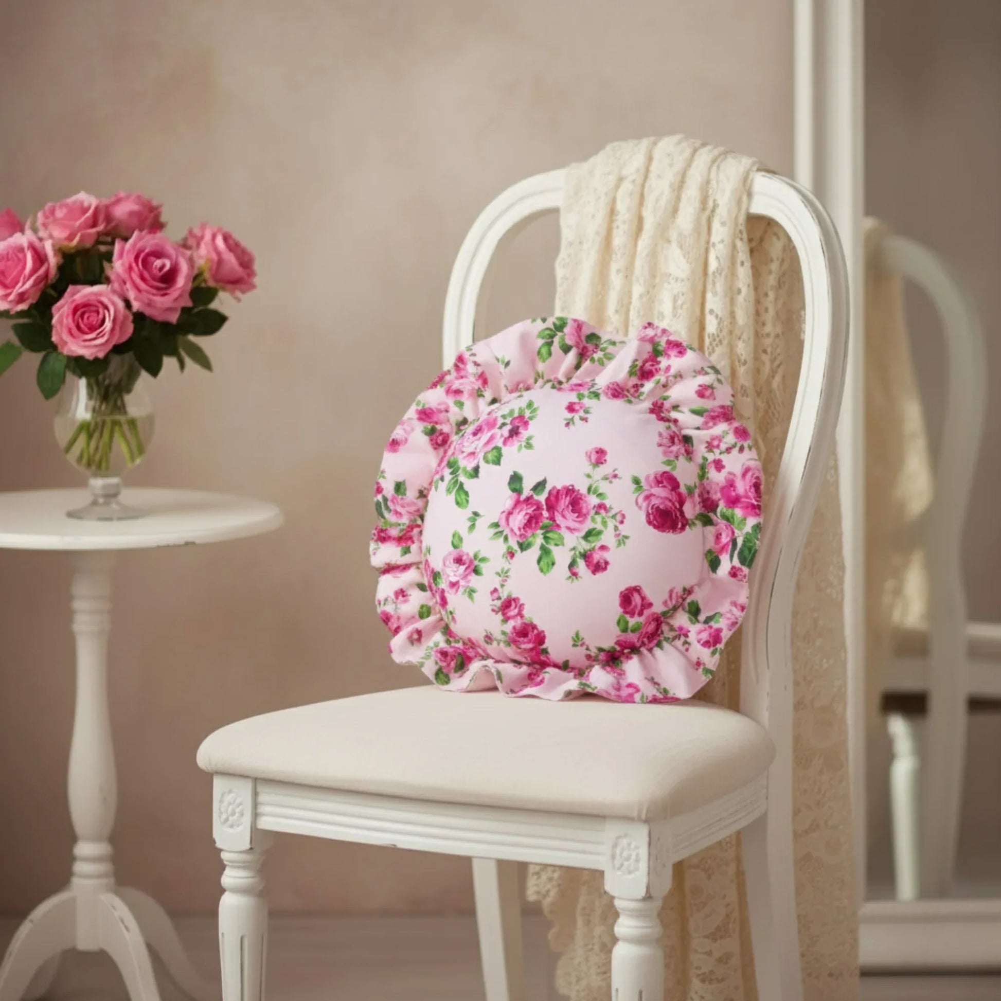 Antique white circular floral cushion on a white chair with a vase of pink roses in the background