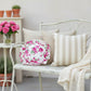 Antique white circular floral pillow on a metallic bench next to metallic tale and transparent vase with flowers on it.