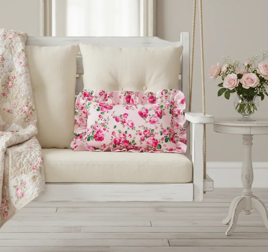 Antique white rectangular floral pillow on a white swing with a vase of flowers in the background