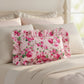 Pale pink rectangular floral pillow with ruffled edge on a bed