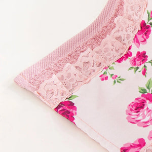 A pink face towel with a floral fleur print and lace detailing, displayed on a white surface.