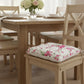 Floral cushion on a wooden chair with a dining table and flowers on in the vase.