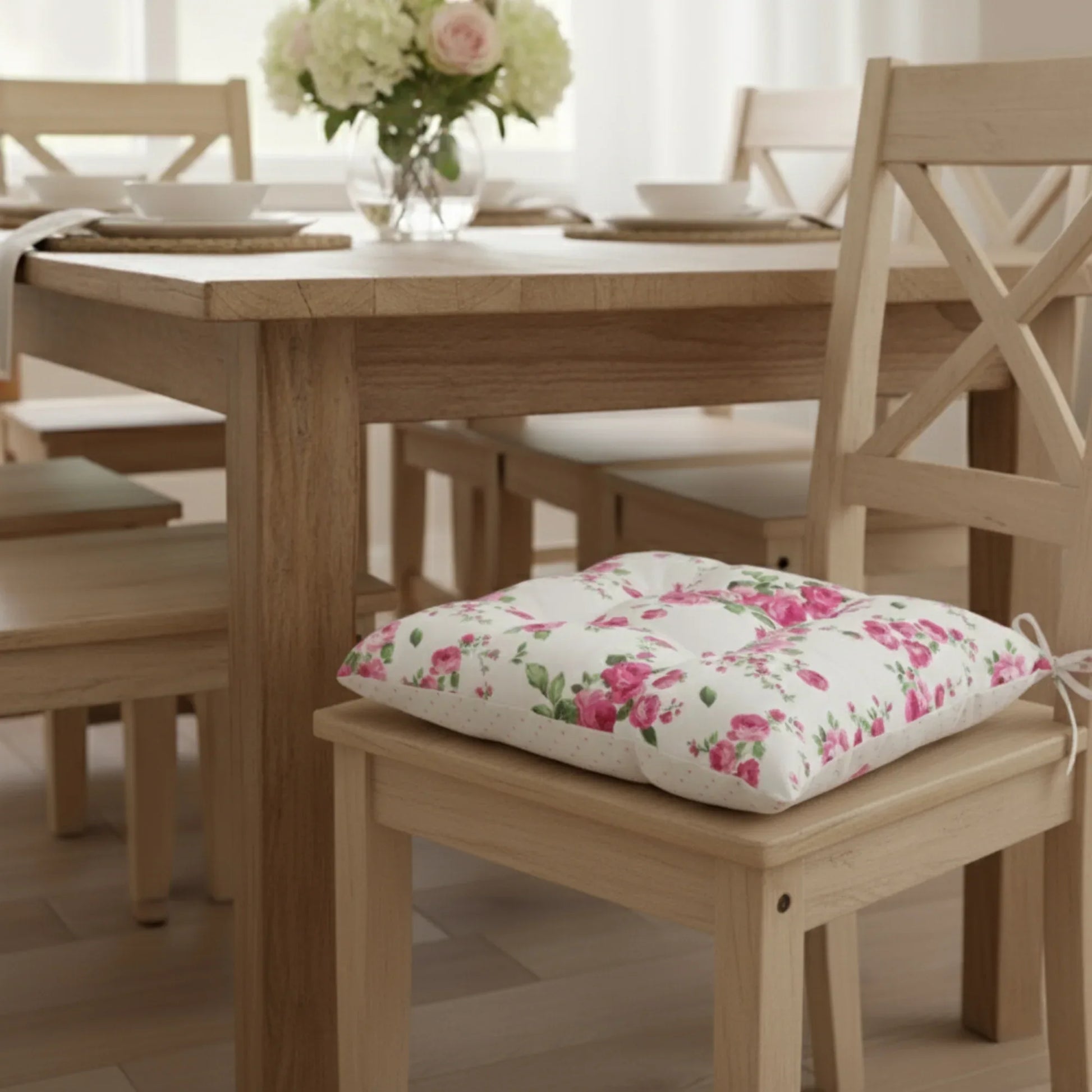 Floral cushion on a wooden chair with a dining table and flowers on in the vase.