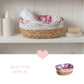 A fleur oval halfa woven basket with a pink rose fabric liner holding a white towel on a white bathroom shelf.