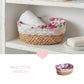 Woven basket with floral lid containing rolled towels on a white shelf.