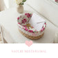 Wicker basket with floral lid on a white surface, featuring keys and an envelope.
