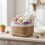Woven basket with floral lace trim containing yarn and knitting tools on a wooden surface.