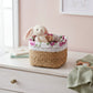 Woven basket with floral liner containing a plush toy on a dresser.