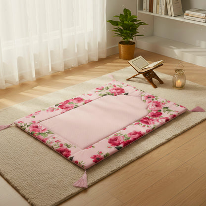 Floral-patterned pink prayer mat on a tatami mat with a wooden stand, Quran, and candle.

