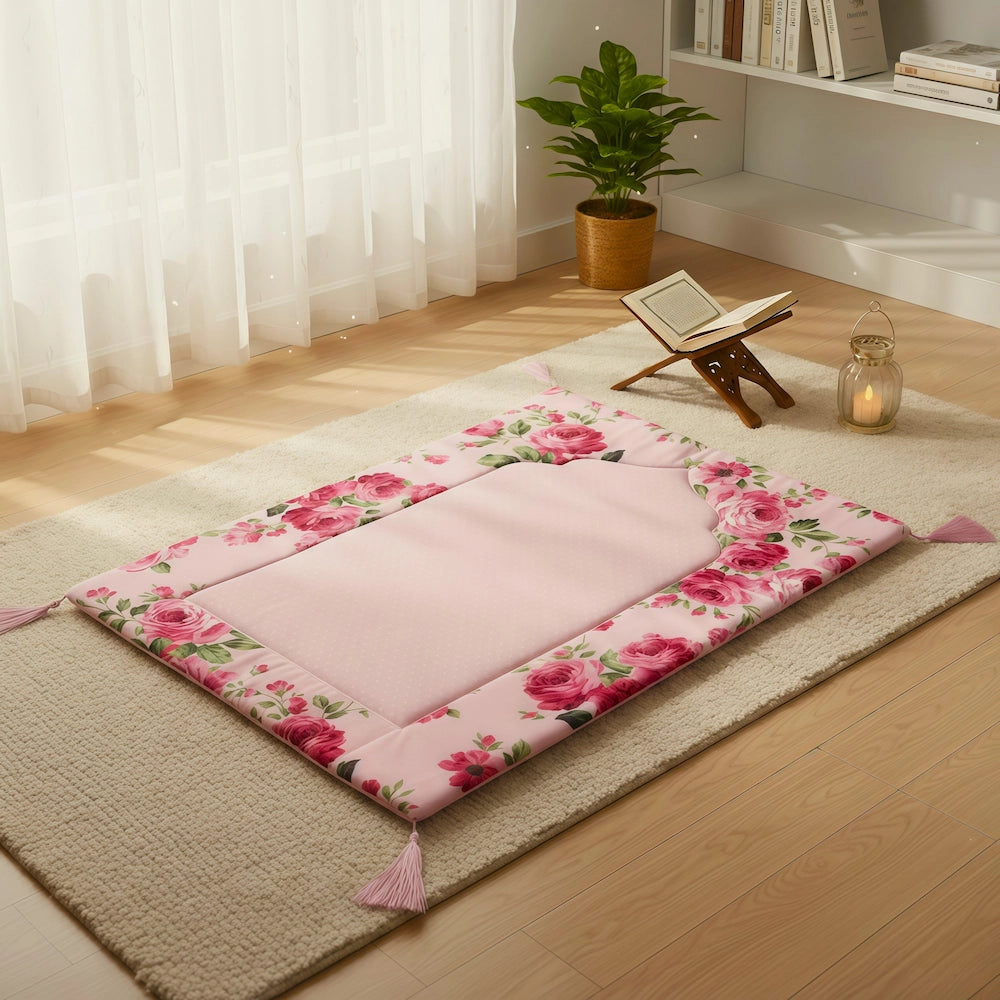Floral-patterned pink prayer rug on a wooden floor with a plant and books in the background