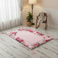 Floral-patterned pink prayer mat on wooden floor with wooden chair, wicker basket, and lamp in the background.