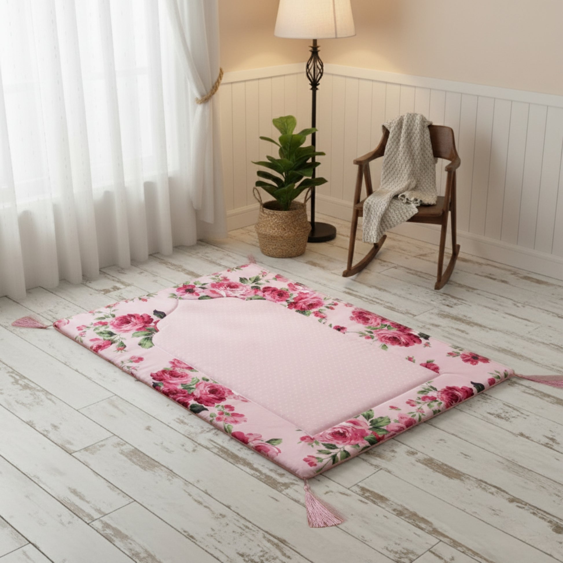 Floral-patterned pink prayer mat on wooden floor with wooden chair, wicker basket, and lamp in the background.