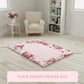 Floral-patterned pink prayer mat on wooden floor with sofa, wooden table on side and vase with flower in it.