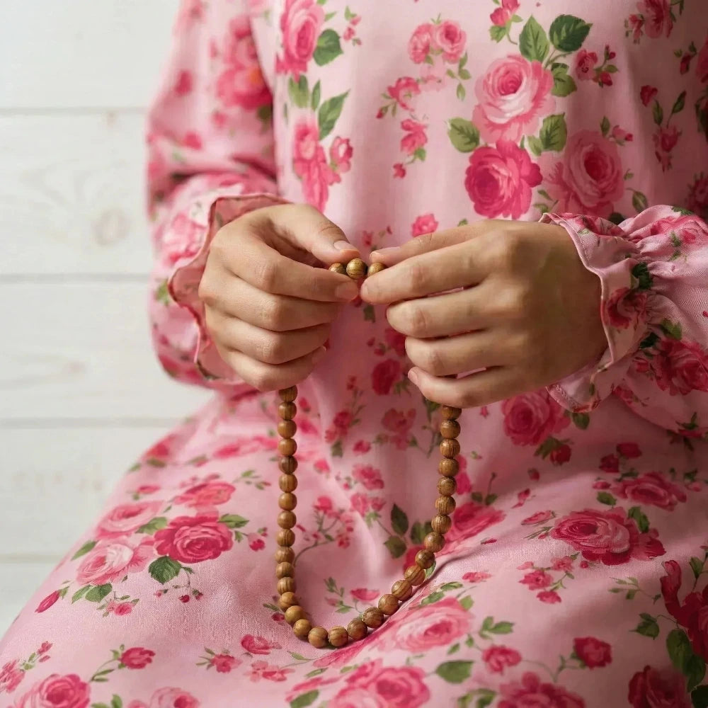 Person wearing a pink floral Isdal Prayer dress holding wooden beads against a white background