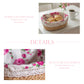 A product detail graphic for a Fleur oval basket featuring a lifestyle shot of bread rolls on a white table and a close-up of the rose print liner and lace edging.