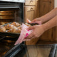 Hands using pink ruffled floral pot holders to remove a baking sheet of golden croissants from a wooden-style oven.