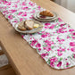 Floral table runner on a wooden table with plates of bread and butter.