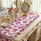 Floral table runner on a vanity with makeup brushes and perfume bottles.