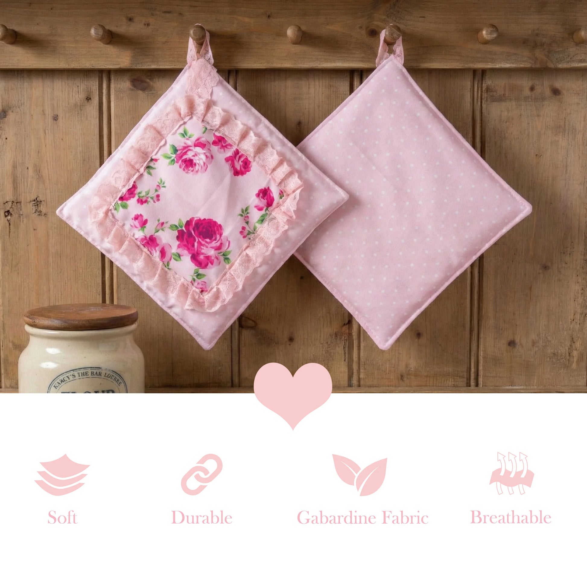 Two pink pot holders hanging on a wooden rack, one with a rose floral print and lace trim, the other with white polka dots.