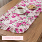 Pink floral ruffled table runner on a wooden table with a white teacup and a small plate of cookies.