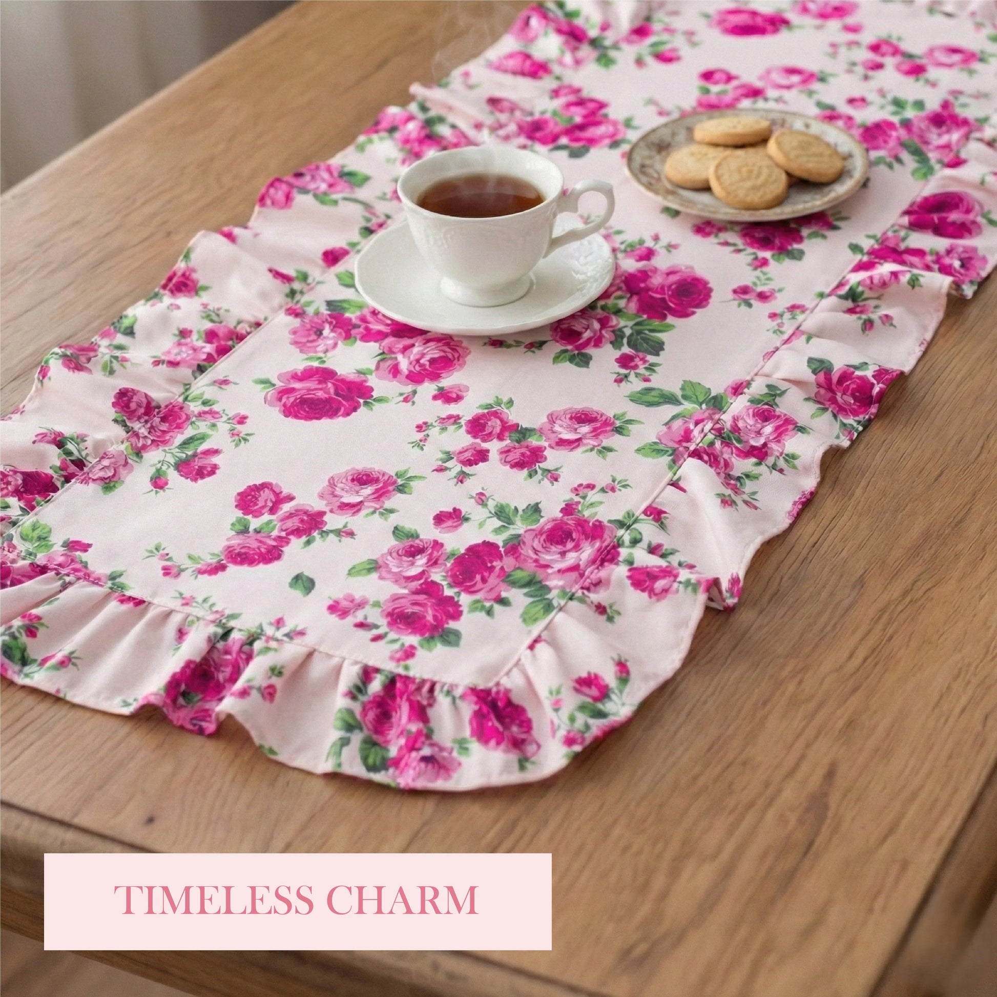 Pink floral ruffled table runner on a wooden table with a white teacup and a small plate of cookies.