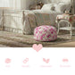 A pink rose fleur pouf in a shabby chic bedroom featuring a white distressed wooden bed frame, patchwork quilt, and vintage wicker side table.