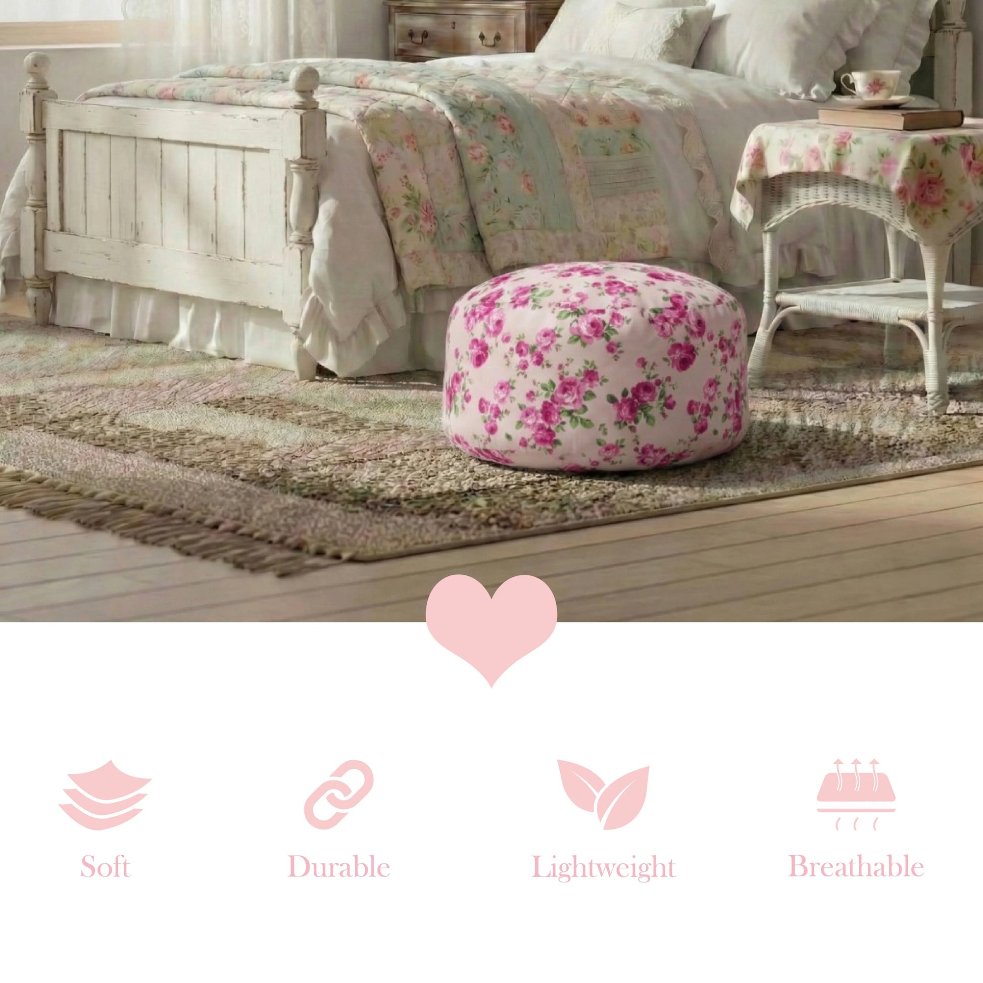 A round fleur pouf with a vibrant pink rose pattern, sitting on a textured area rug at the foot of a white distressed wooden bed frame in a sunlit bedroom with a vintage wicker side table.