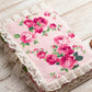 Floral fabric with pink roses and green leaves on a pink background, featuring lace trim.