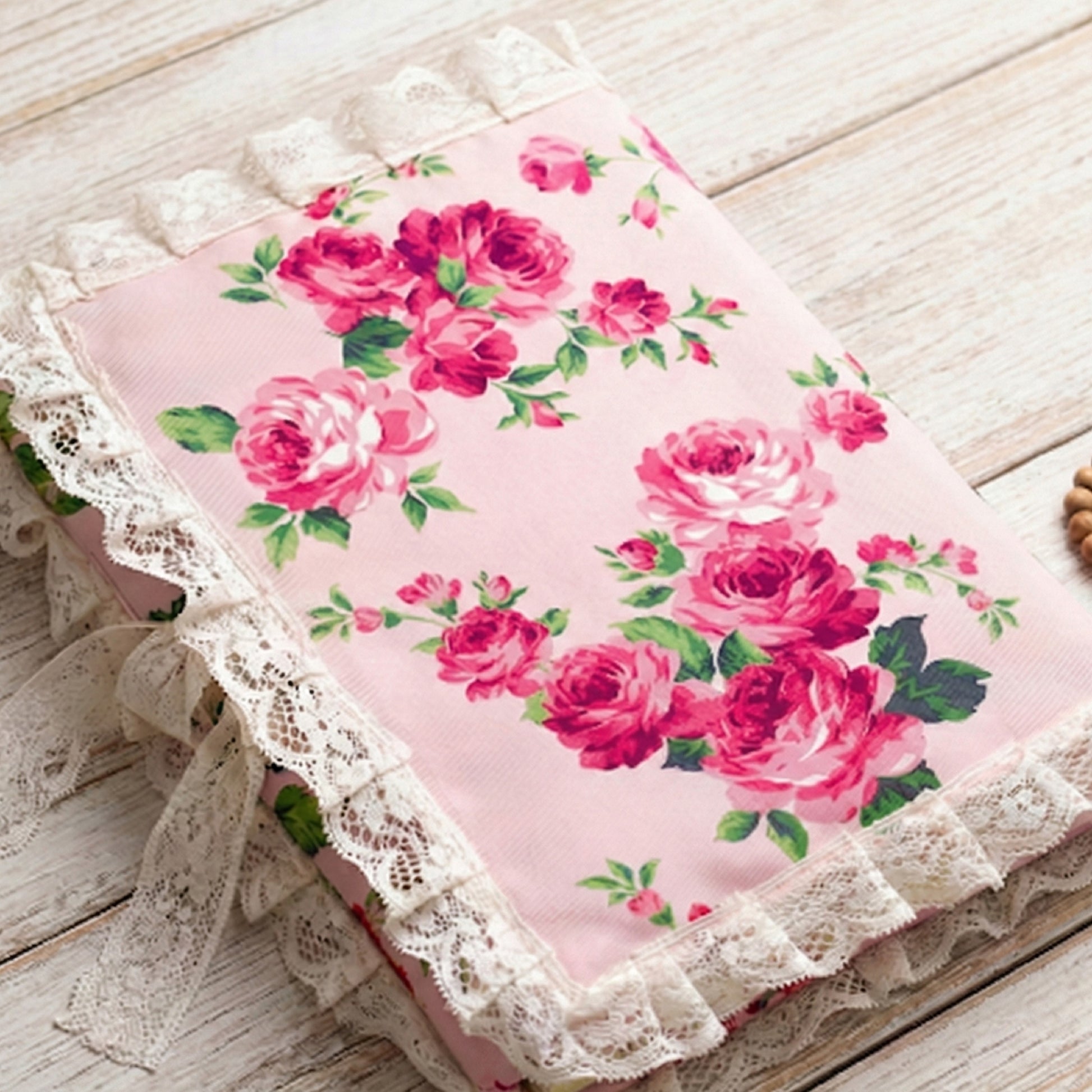 Floral fabric with pink roses and green leaves on a pink background, featuring lace trim.