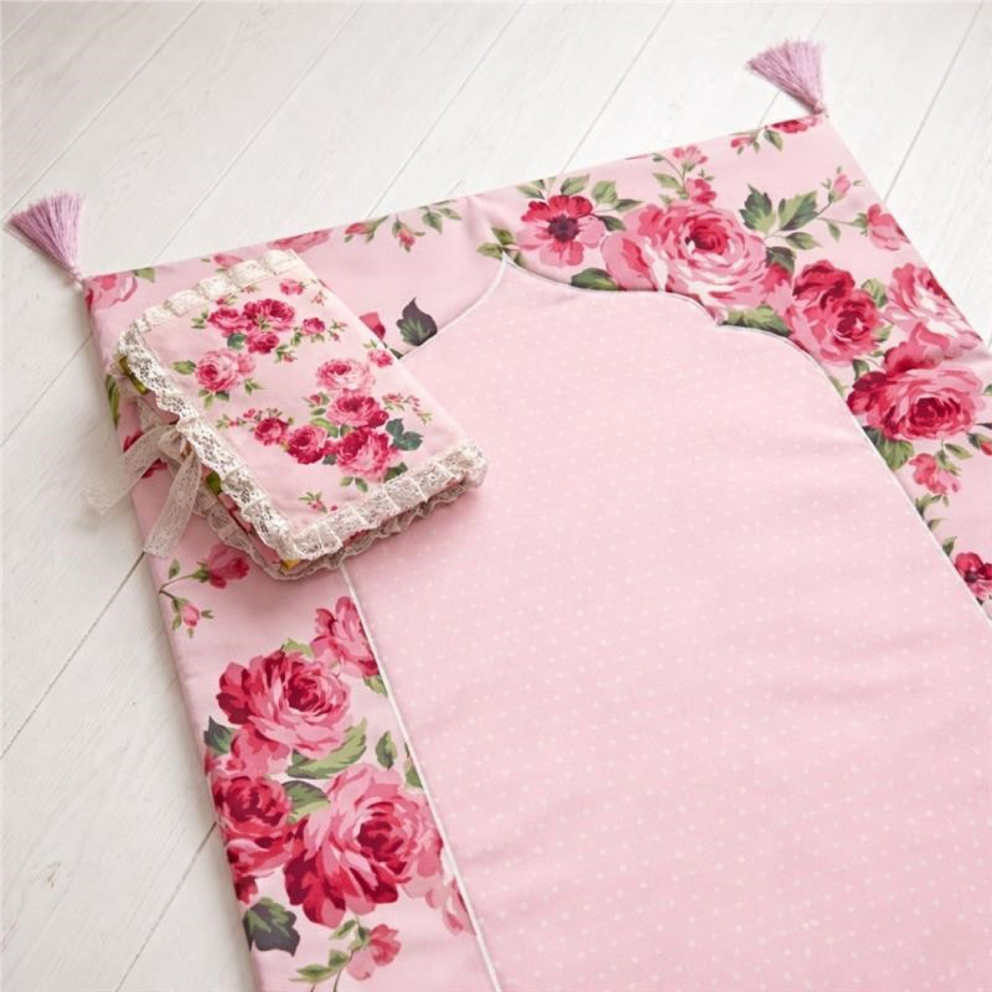 Pink fabric fleur Quran cover on floral patterns padded prayer mat on a white wooden floor