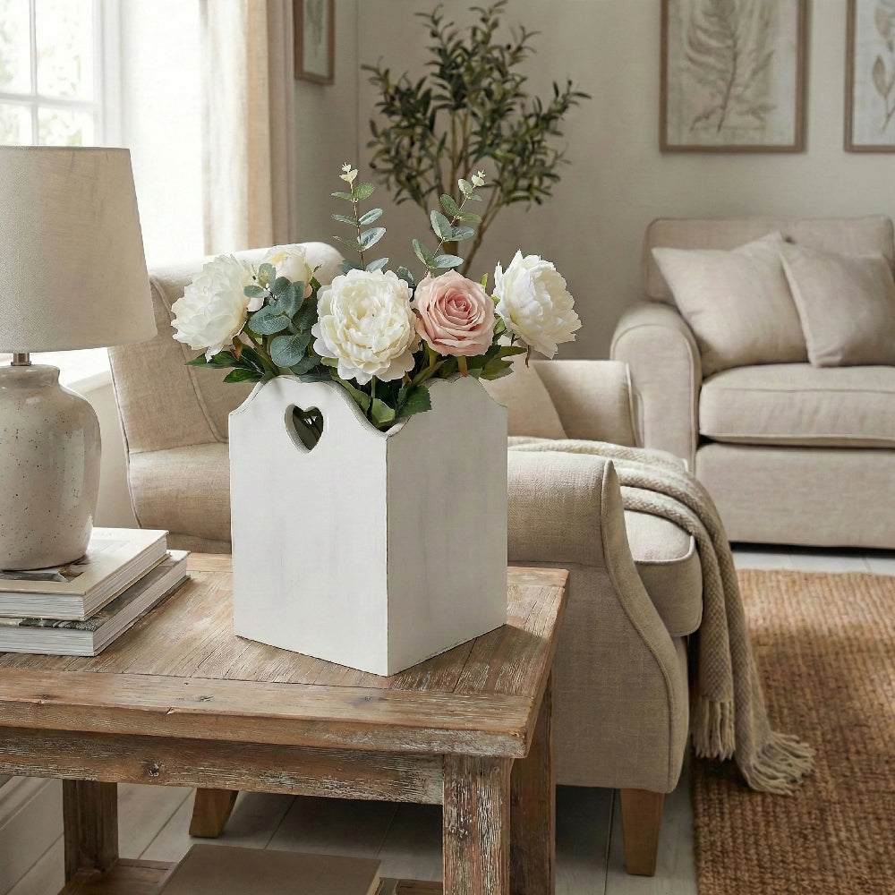 Floral arrangement in a white wooden basket on a wooden table in a living room.