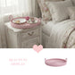 Floral bedding and a pink woven wicker tray with a tea set on a white nightstand.