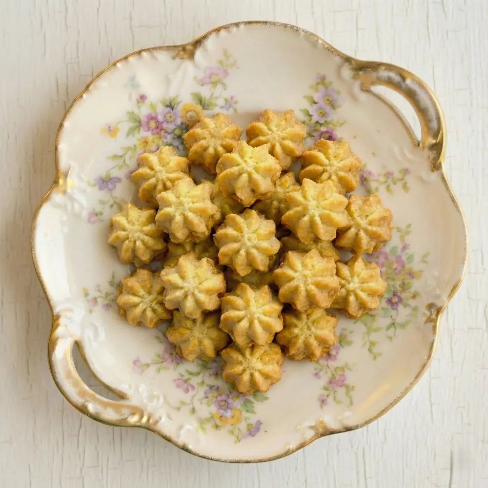Decorative plate with floral patterns holding petit four cookies on a light wooden surface.