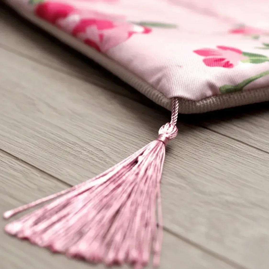 Floral-patterned prayer rug with a tassel on a wooden surface