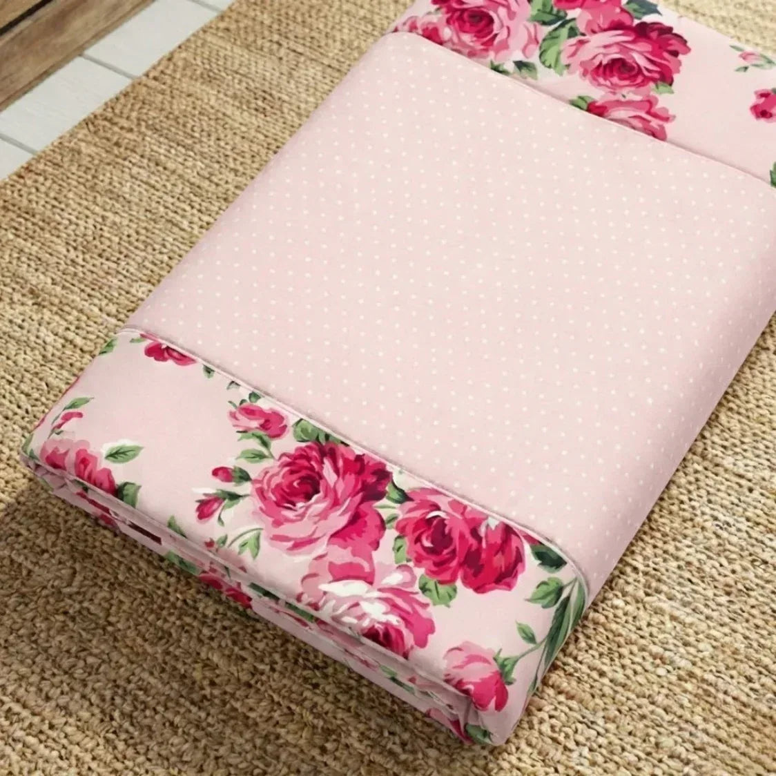 Floral-patterned pink fabric prayer rug roll on a textured surface