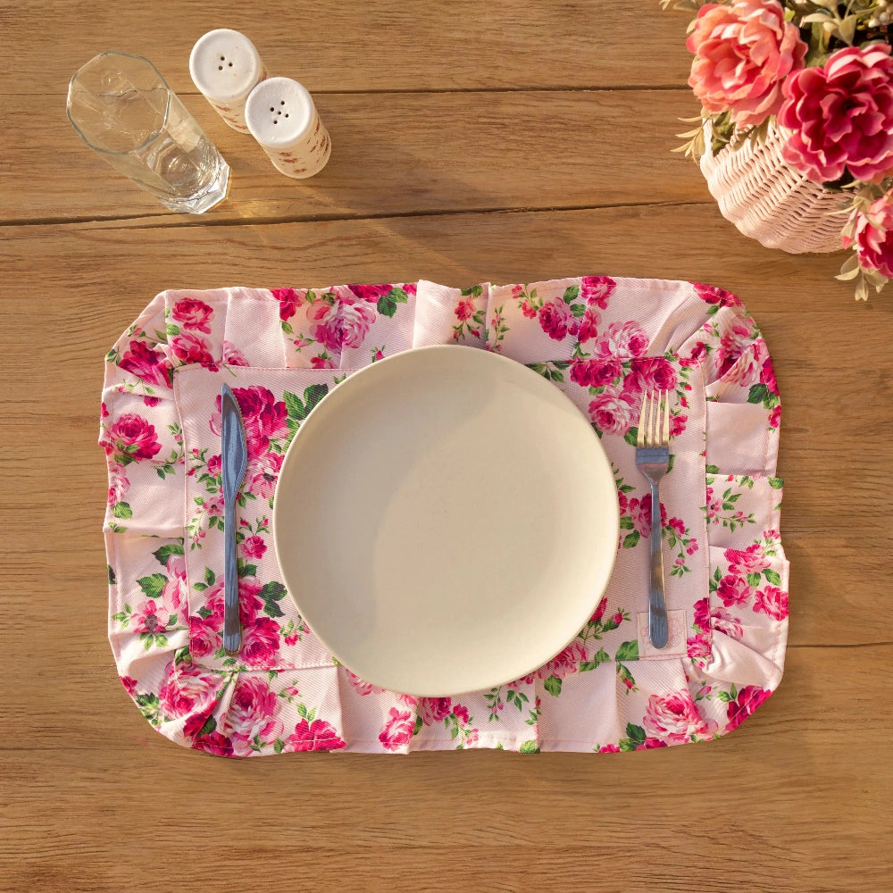 Floral placemat with a plate, cutlery, and glasses on a wooden table.