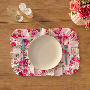 Floral placemat with a plate, cutlery, and glasses on a wooden table.