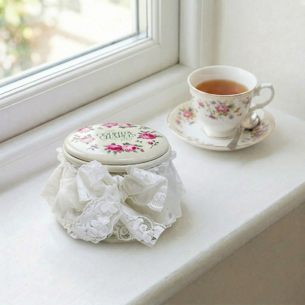 Teacup with floral design on a saucer next to a decorative box with lace on a windowsill.
