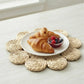 Flower-shaped woven placemat featuring spiral petal details, topped with a white plate of croissants and a bowl of fresh berries.