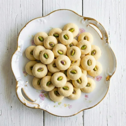 Decorative plate with ghorayeba cookies and pistachios on a white wooden surface
