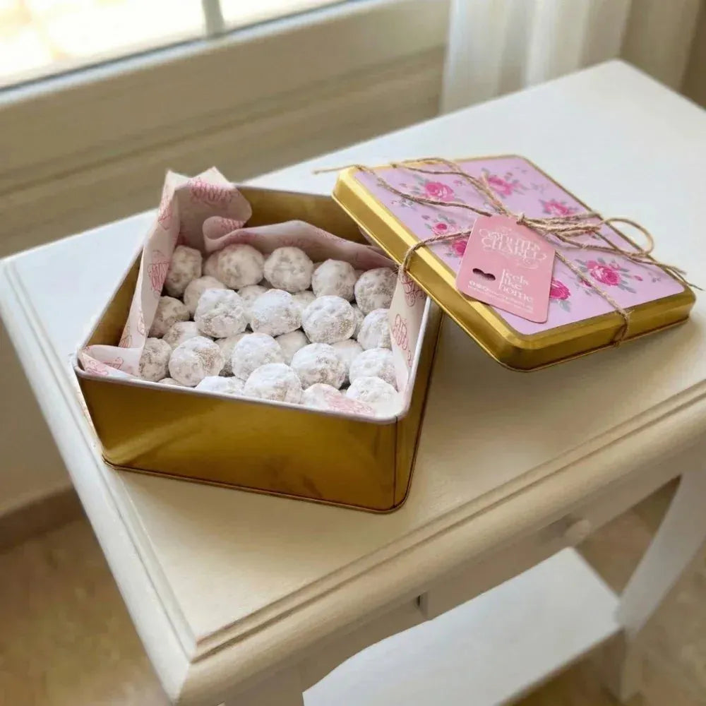 Gold tin filled with powdered sugar cookies on a white surface