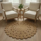 Round rug in front of two beige armchairs with a small wooden table and plant in a bright room.