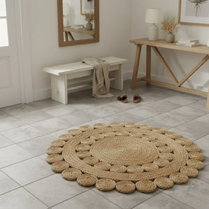 Round woven rug on a tiled floor with wooden furniture and decor.