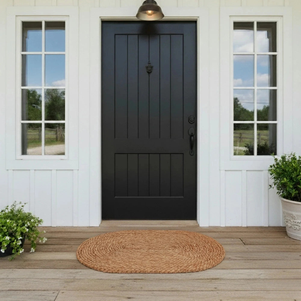 Black front door of a house with a wooden deck and round jute rug.