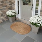 Front door with a woven mat, potted white flowers, and stone wall.