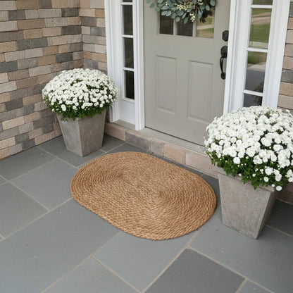 Front door with a woven mat, potted white flowers, and stone wall.