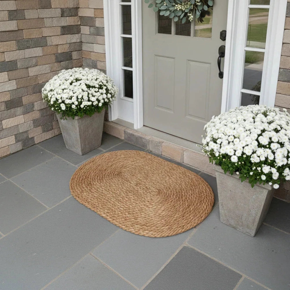 Front door with white flowers in planters and a woven mat on a stone patio.