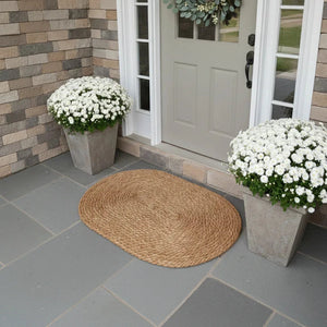 Front door with white flowers in planters and a woven mat on a stone patio.