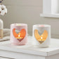 Two heart-shaped candle holders with candles inside on a white surface.