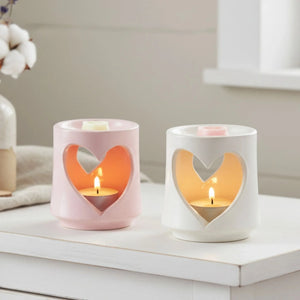 Two heart-shaped candle holders with candles inside on a white surface.